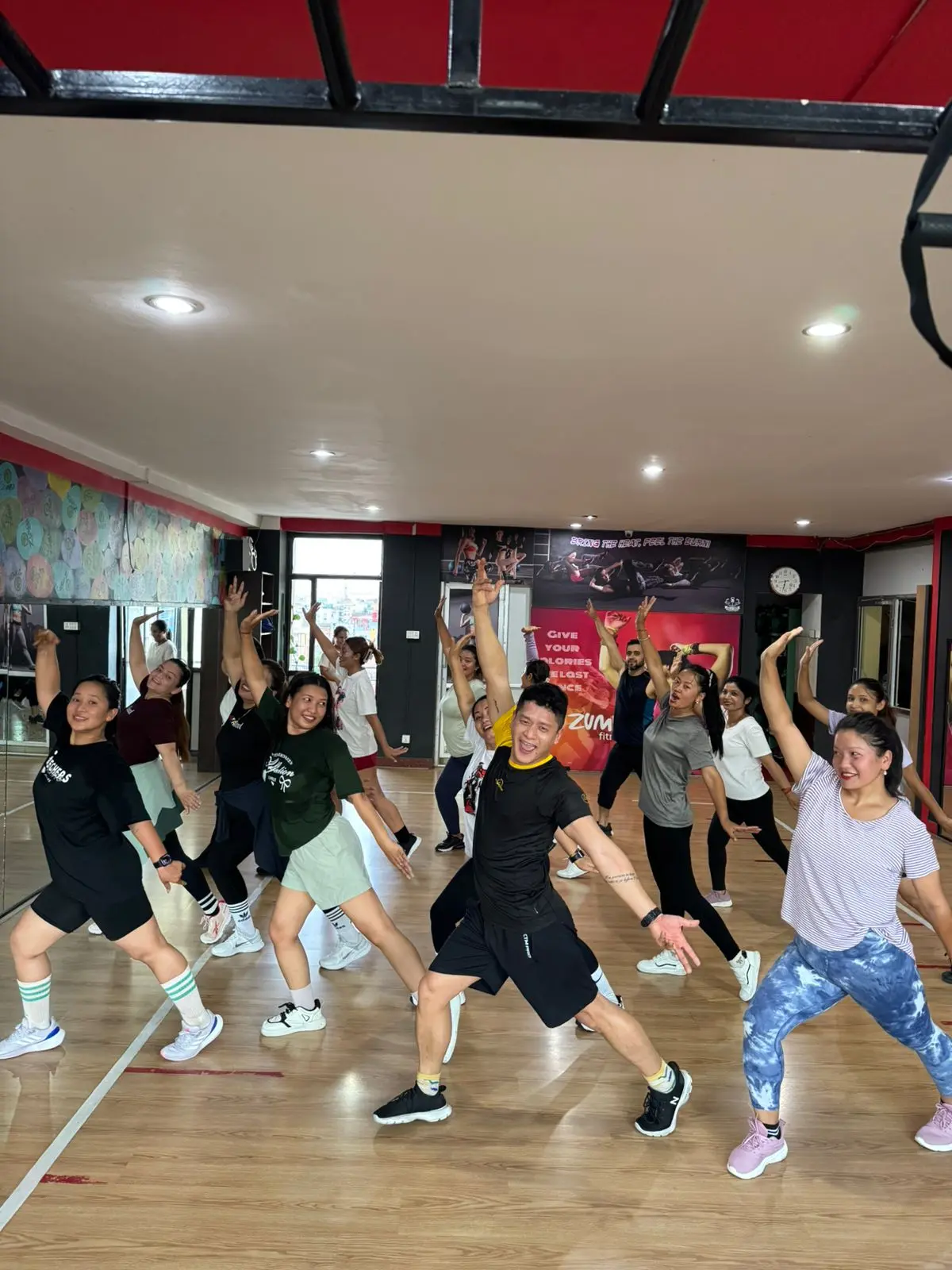 Energetic Zumba class at Muscle Mania with 10+ members and male instructor on wooden floor